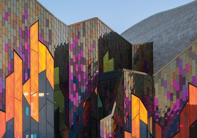 Vue extérieure d’un édifice dont les fenêtres aux lignes anguleuses sont parées d’un verre dichroïque 3M aux reflets chaleureux.