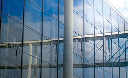 Large window-covered building reflecting blue sky and clouds.
