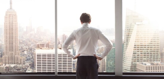 Un homme regardant par une fenêtre donnant sur la ligne d'horizon de la ville.
