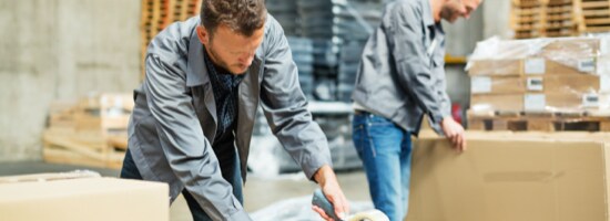 Two men sealing boxes in a fulfillment centre.
