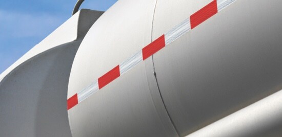 A transport truck tanker trailer with red and white conspicuity tape running down the side.

