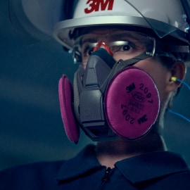 A worker wearing a white hard hat with the 3M logo and a respirator mask with pink filters.