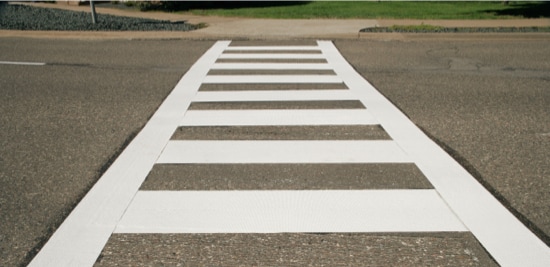 Low-angle shot of white painted crosswalk across road.
