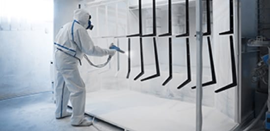A person in a bunny suit spraying metal with a powder coat.
