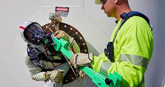 Front view of two workers with one exiting a confined space.
