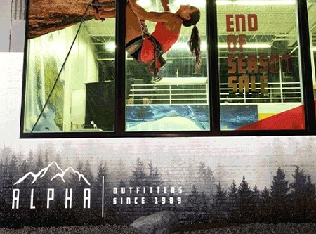 Exterior of retail store at night with printed window graphics and retroreflective film on brick printed with tree motif and logo.
