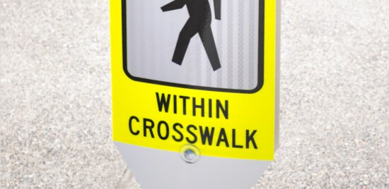 Yellow sign with letters and symbols reading “State law: Yield to pedestrians in crosswalk.
