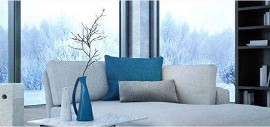 A white couch in front of two large windows showing a backyard covered in snow.
