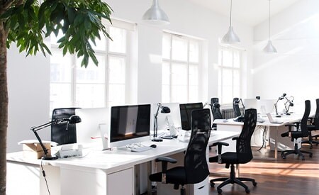 Un espace de bureau moderne, épuré et lumineux, doté d’un mur de fenêtres laissant pénétrer la lumière naturelle.
