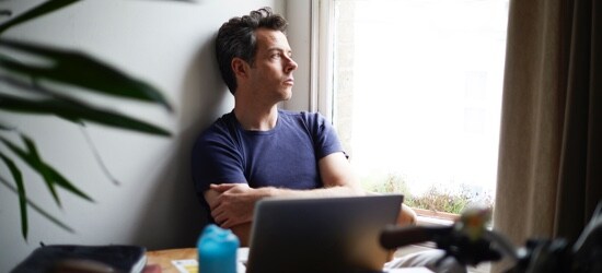 A man looking out of his home window.
