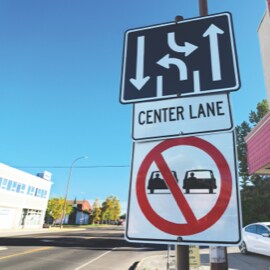 Stacked road signs depicting driving and turn lanes, center lane, and prohibited parallel driving.