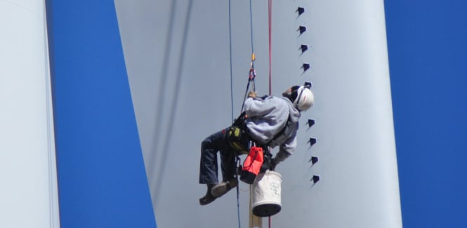 Un ouvrier suspendu en hauteur installant des générateurs de tourbillons 3M.
