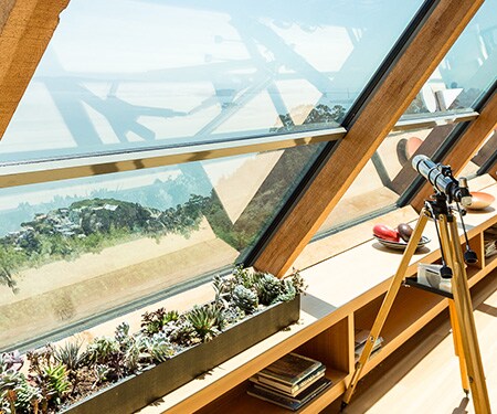Interior of home with large angled windows looking out on beach and blue sky.
