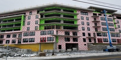 Multi-story building under construction, featuring exposed insulation and weatherproofing materials, with a crane positioned nearby.
