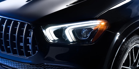Close-up of a dark SUV’s front, showing an LED headlight, amber corner light, and grille.
