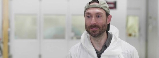 Un travailleur d’atelier de carrosserie portant une combinaison et un chapeau à l’envers.
