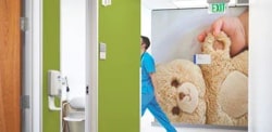 Le mur d’un couloir d’hôpital avec une pellicule graphique sur un mur représentant une main de bébé tenant un ours en peluche.
