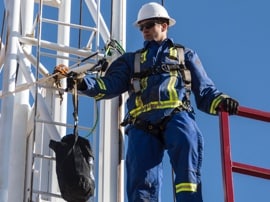 A worker wearing fall protection gear and clothing with reflective material.