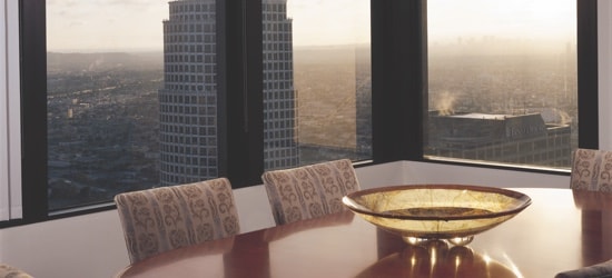 A kitchen table in an apartment building, with the windows overlooking a city skyline.
