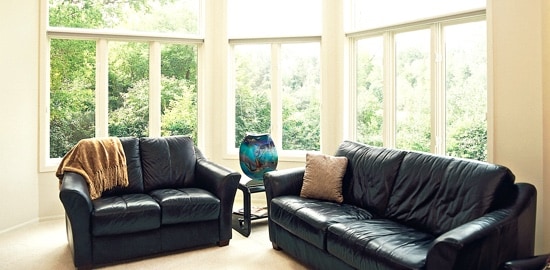 A living room with two leather couches and windows overlooking a forest.
