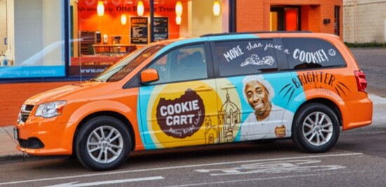 A fleet minivan wrapped in an orange wrap with branding for a company called the Cookie Cart.
