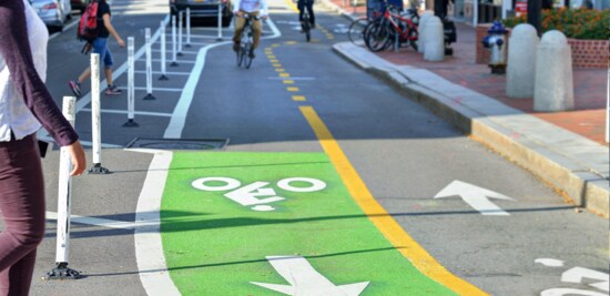 Man on a scooter using a protected bike lane in an urban city street.
