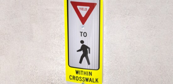 Standalone sign with symbols and letters to create the message 'State law: Yield to pedestrians within crosswalk'.
