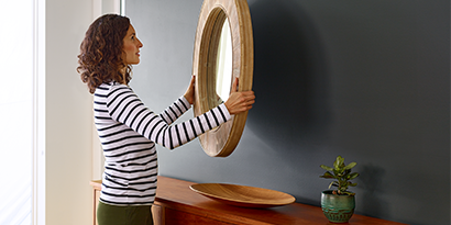 A woman hanging a large mirror on a wall.
