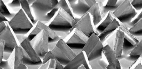 Vue microscopique des grains abrasifs de forme de précision d’un minéral de la marque Cubitron(MC) II qui ressemblent presque à des pyramides d’argent dans un motif non aléatoire.
