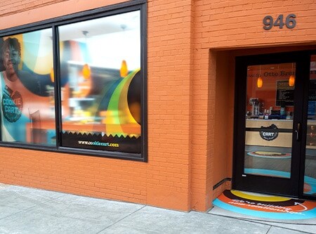 Orange brick building exterior with graphic films on windows and sidewalk.
