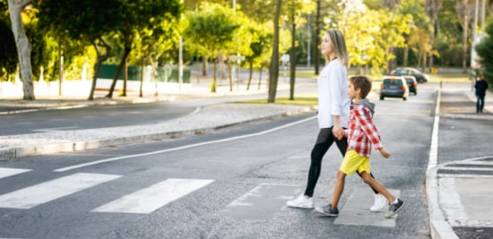 Une femme et son enfant qui traversent la rue avec confiance sur un passage piéton en section courante doté d’une avancée de trottoir et de lignes peintes.

