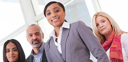 Four individuals appear to be in a professional setting, possibly an office or a business meeting.
