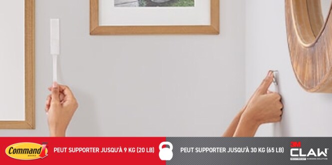 Deux mains installent un système d’accrochage mural  la gauche tient une bande Command, la droite utilise une suspension CLAW 3M pour cloisons sèches.
