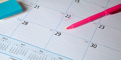 Un grand calendrier de bureau avec surligneur rose posé sur le dessus avec une date encerclée.

